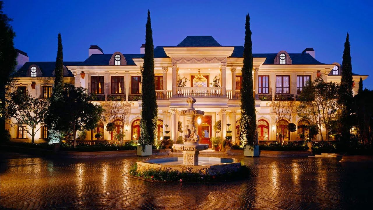A grand illuminated residence at dusk with a fountain courtyard